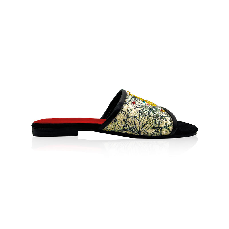 side view of black and white canvas slip on sandals with gold stitching and colored hand embroidered beads. Red leather interior and black leather toes